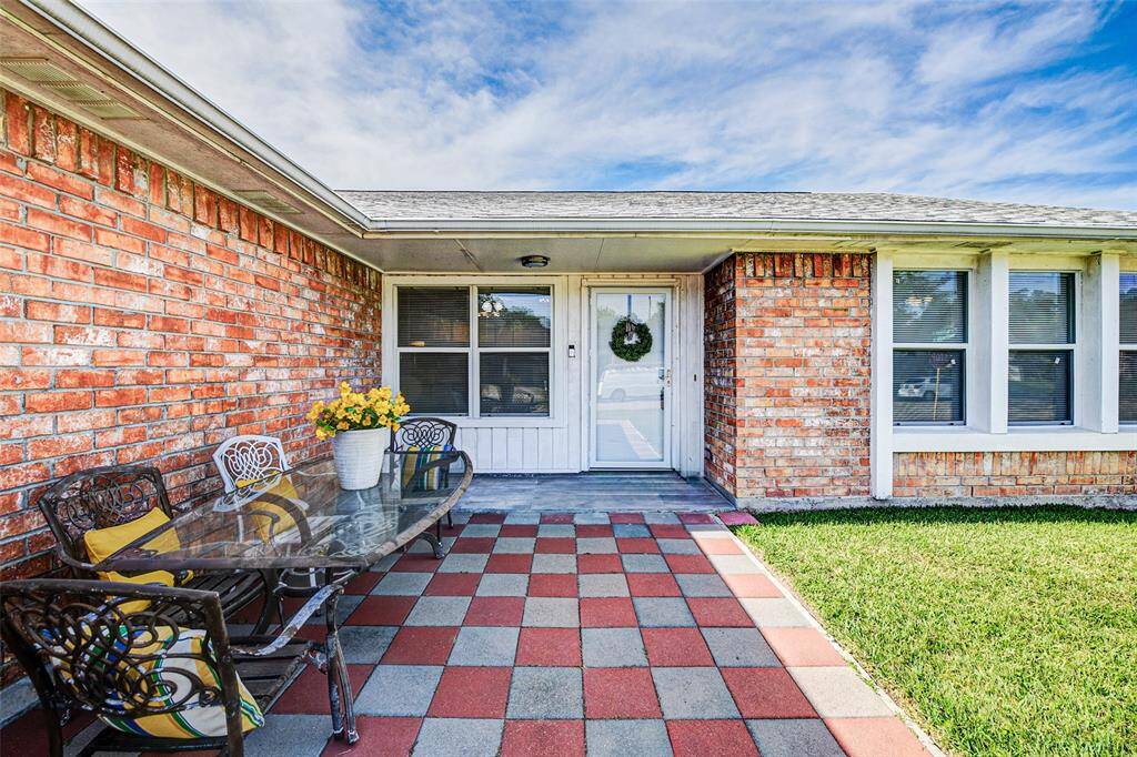 A welcoming front porch features a checkered tile pattern. The outdoor seating area includes decorative iron chairs and a glass table which will stay with the home. It's perfect for eating outside.
