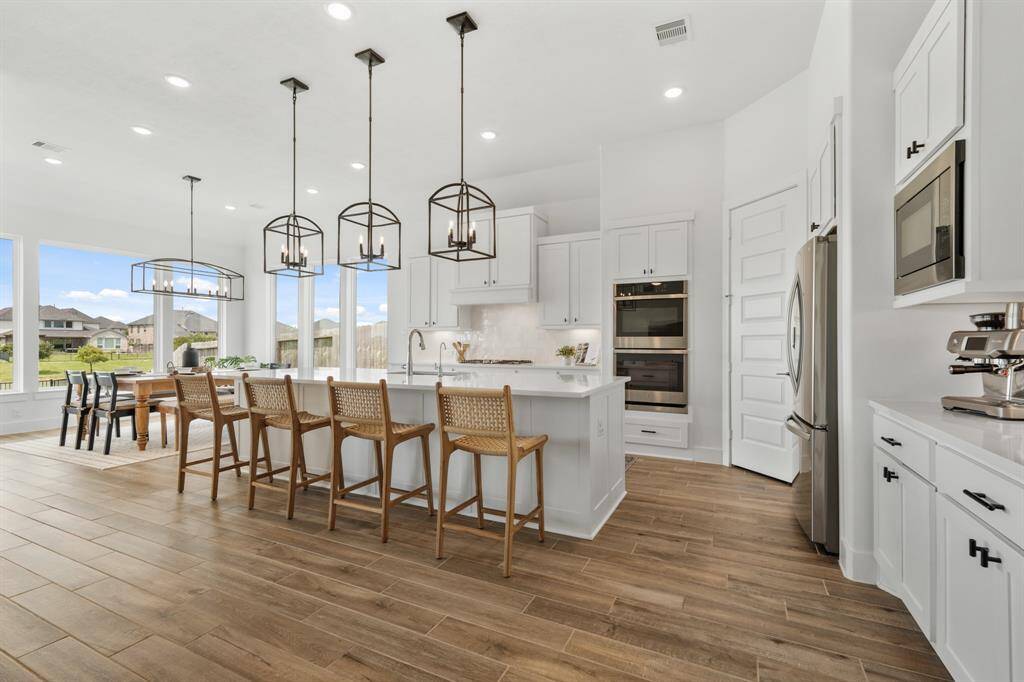 At the heart of the home, this stunning kitchen boasts a spacious, thoughtfully designed layout ideal for entertaining. The centerpiece is a magnificent island with ample seating, illuminated by three striking Pottery Barn iron pendant lights that add warmth and rustic elegance to the space—perfect for gathering with friends and family.