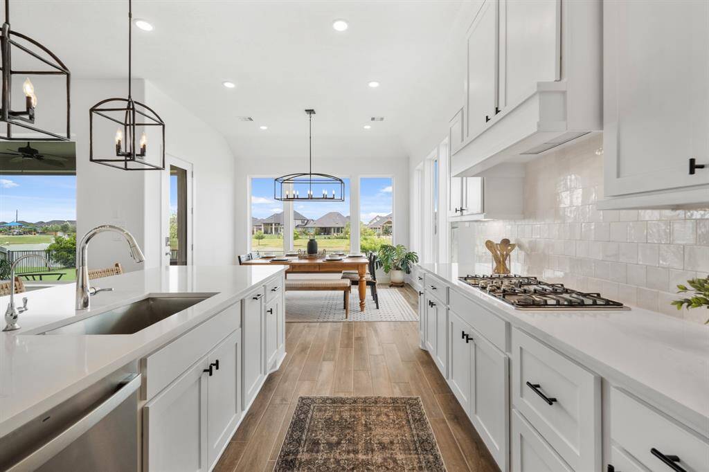 The backsplash features a sophisticated running bond pattern with Marazzi Zellige Gesso tile, perfectly complementing the JKraft Studemont Pure White painted cabinets. A sleek gas cooktop with a coordinating vent hood provides a seamless look, while 12-inch LED undercabinet lighting brightens the workspace.