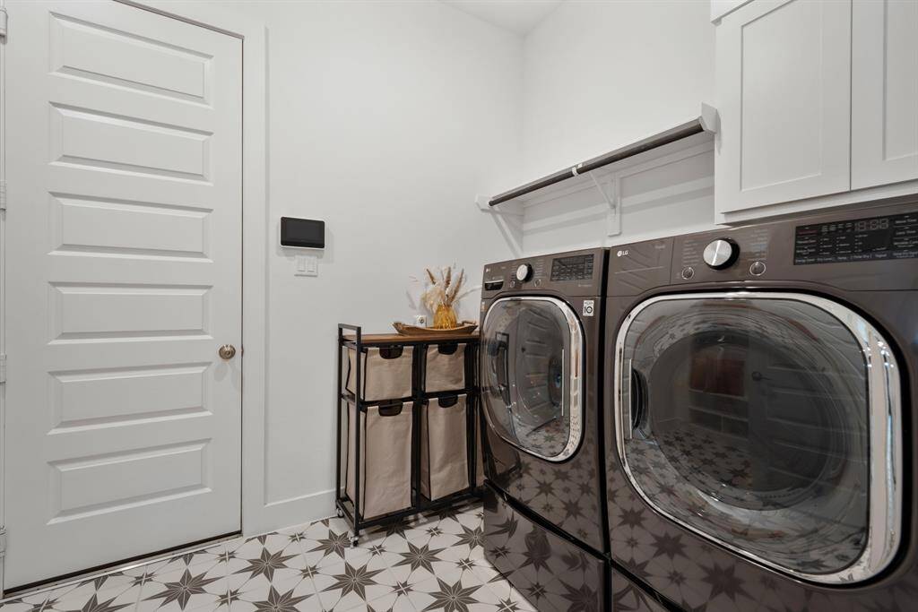 The dedicated laundry room includes full-sized washer and dryer connections, upper cabinetry, and a hanging rod for added utility. Designed tile flooring and ample space make it a highly functional and efficient work area.