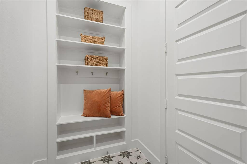 A custom built-in mud bench offers convenient storage and organization, complete with upper shelving, coat hooks, and cubbies below. This drop zone is perfectly located for managing shoes, bags, or coats near the home’s entryway.