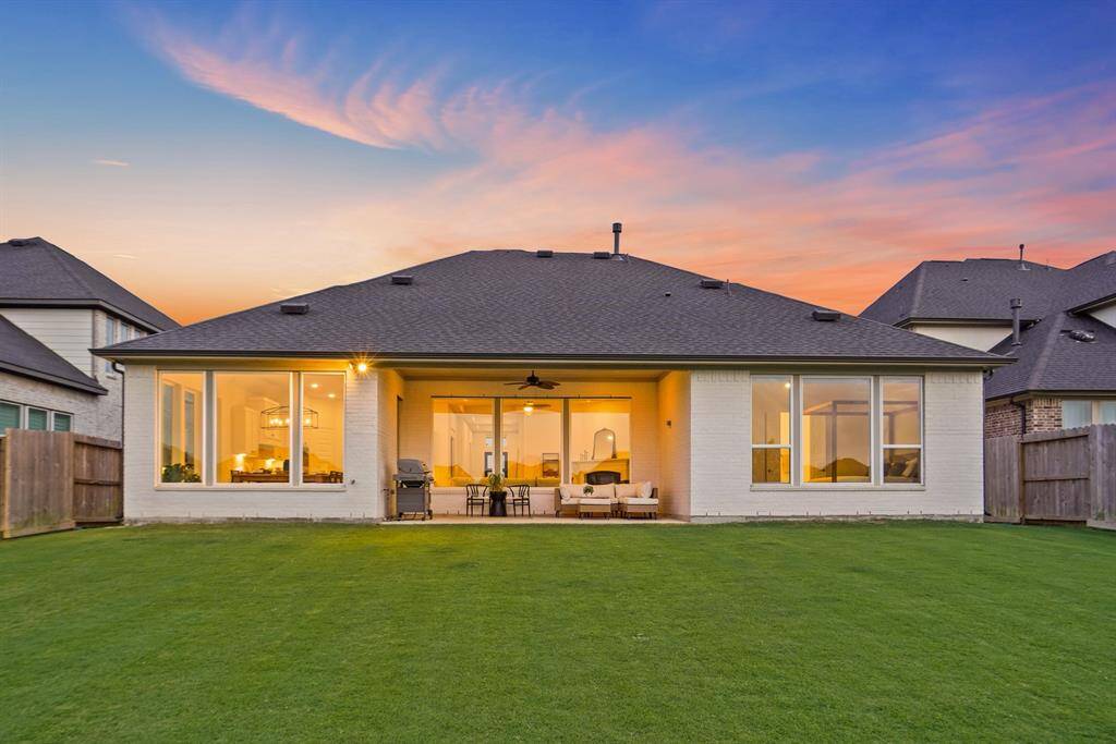 This home features a spacious covered back patio with recessed lighting and a ceiling fan, perfect for year-round outdoor use. Expansive windows line the rear elevation, offering abundant natural light and uninterrupted views of the backyard and beyond.