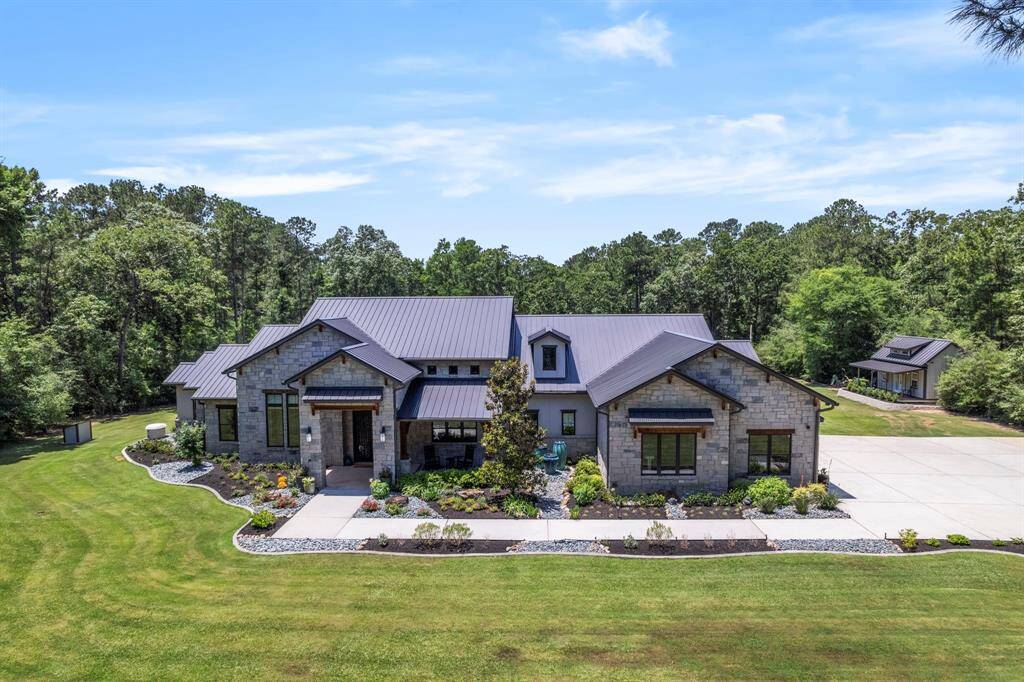From above, the estate’s beautifully manicured grounds come to life—lush green lawns stretch across the front of the property, bordered by thoughtfully designed flower beds, river rock accents, and curved concrete edging that frames the home with elegance.