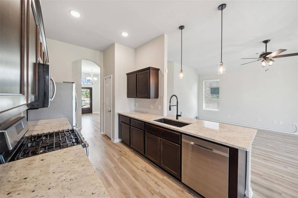 Experience culinary luxury in this chef's kitchen featuring mahogany stained cabinets, granite countertops, subway tile, Samsung stainless steel appliances, a 5-burner gas range, and elegant pendant lighting over the breakfast bar.