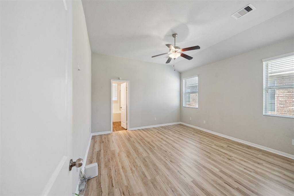 Expansive primary bedroom with modern features that include neutral paint color, high ceilings, LVP flooring, ceiling fan, and ensuite bathroom and walk-in closet.