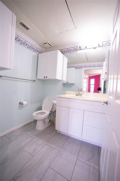 This bathroom features light blue walls with floral trim, white cabinetry, and a modern vanity. It has tiled flooring, a standard toilet, and ample lighting, providing a clean and bright space.