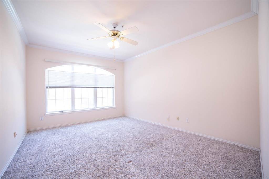 This bright room features soft carpet, a large window offering ample natural light, and a ceiling fan for added comfort. The neutral walls create a versatile space, ready for personal touches.