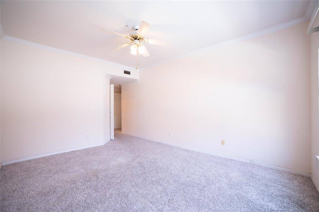 This room features neutral walls, plush carpet, a ceiling fan, and ample natural light from a large window, creating a bright and welcoming space.