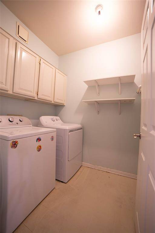 Compact laundry room with a washer and dryer, overhead cabinets, and wall shelves for storage. Neutral colors and bright lighting.