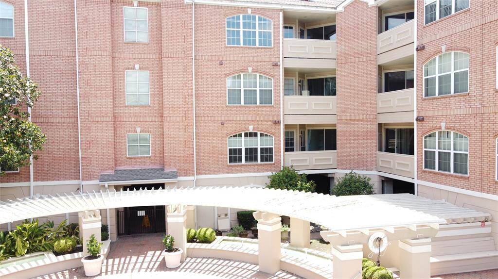 This photo shows a multi-story brick apartment building with large windows and a central courtyard. The courtyard features a decorative pergola and landscaped greenery, offering a welcoming and open atmosphere.