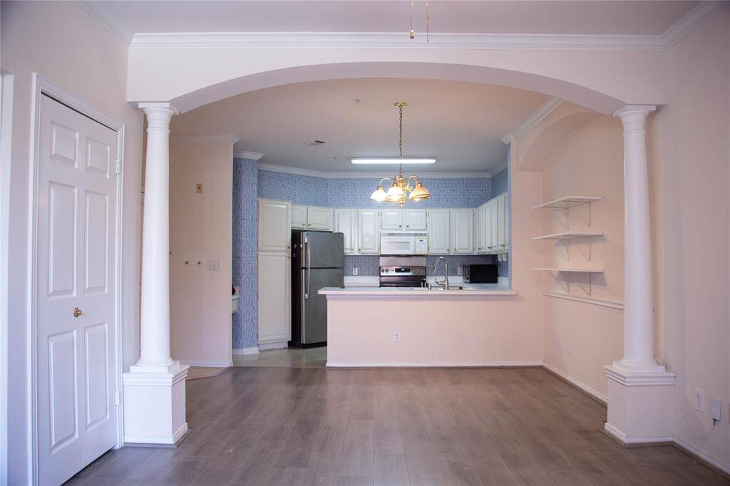 This photo showcases a bright, open-concept kitchen and living area. The kitchen features white cabinetry, stainless steel appliances, and a breakfast bar. The living space has elegant columns, built-in shelves, and hardwood flooring, creating a welcoming atmosphere.