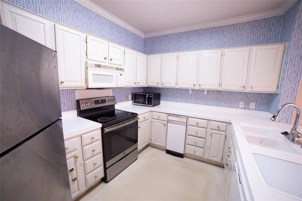This kitchen features white cabinetry with ample storage, modern appliances including a stainless steel refrigerator and a black stove, and a spacious countertop. The blue patterned backsplash adds a touch of style, and there's a double sink for convenience.