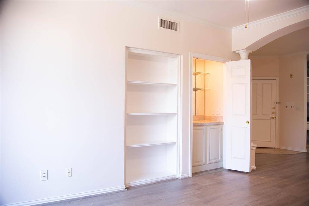 This photo shows an entryway with light-colored walls and flooring. It features an open door leading to a small nook with shelves and cabinetry. The area is bright and has built-in shelves for storage, contributing to a clean and welcoming space.