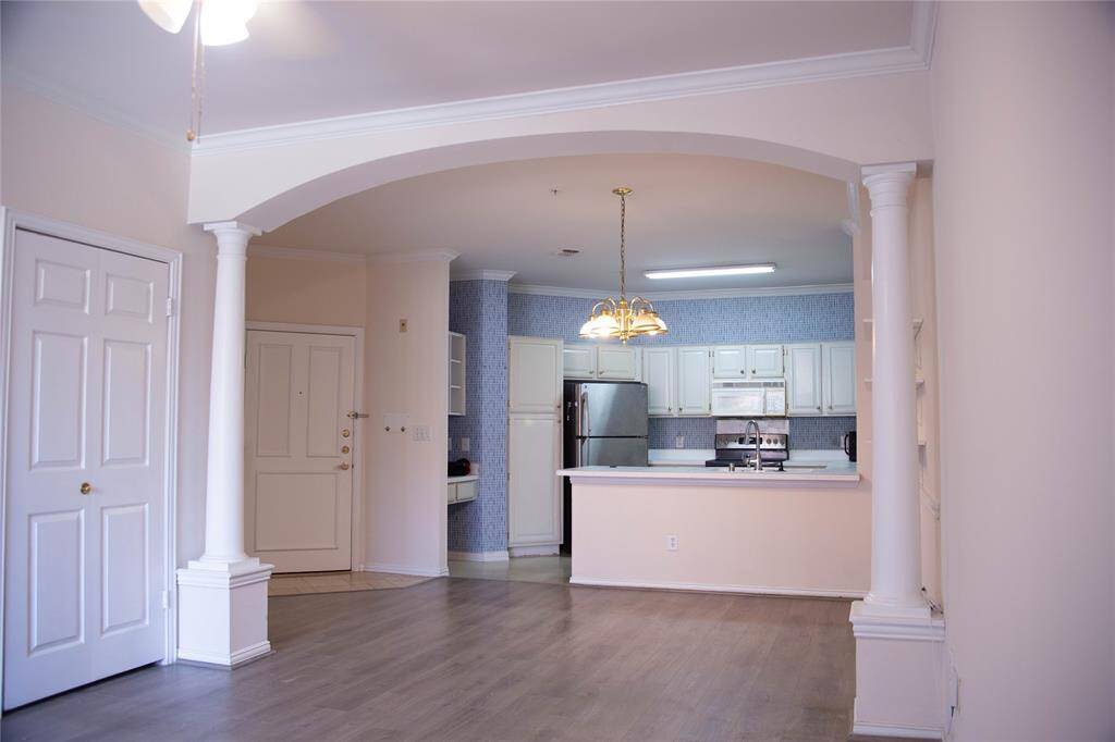 Bright open-plan kitchen and living area featuring elegant columns, stainless steel appliances, and ample cabinet space, complemented by light wood flooring.