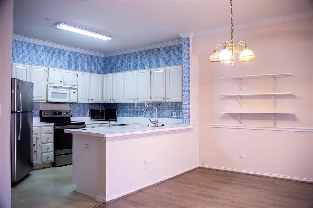 This photo showcases a modern kitchen with white cabinetry, stainless steel appliances, and a blue tile backsplash. It features a breakfast bar that opens to a dining area with built-in shelving and a stylish chandelier. The space is bright and inviting, perfect for entertaining.