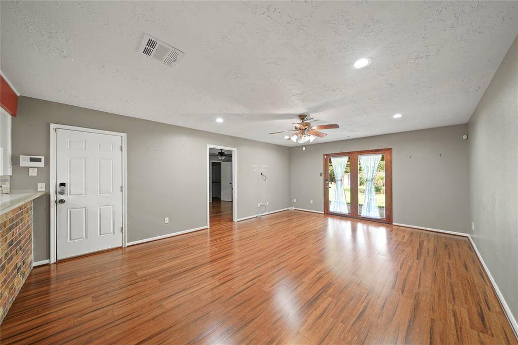 Photo shows the living area with double doors that lead to the backyard. White closed door leads to the 2 car garage and the open door leads to the primary bedroom.