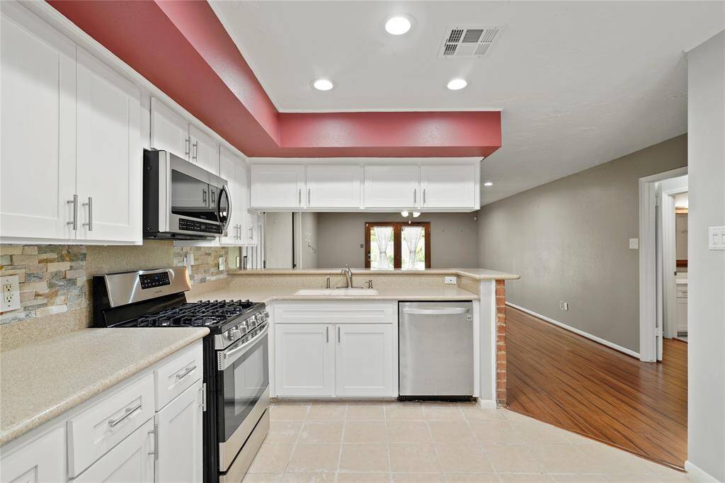 Modern kitchen with white cabinets and stainless steel appliances. Features a spacious layout with recessed lighting, and an open view to the living area.