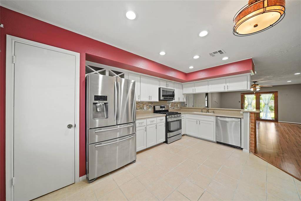 This modern kitchen features stainless steel appliances, white cabinetry, and a stylish red accent wall. It opens into a spacious living area with wood vinyl flooring and ample natural light.