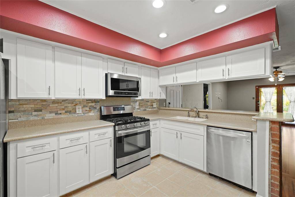 This modern kitchen features sleek white cabinetry, stainless steel appliances, and a stone tile backsplash.