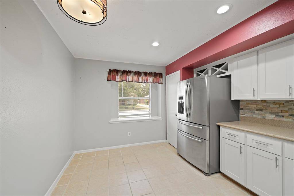 Bright kitchen space with modern stainless steel appliances, white cabinetry, and a stone backsplash. It features a window with a view outside, recessed lighting, and a charming light fixture. Space is large enough for breakfast/ small dinning area.
