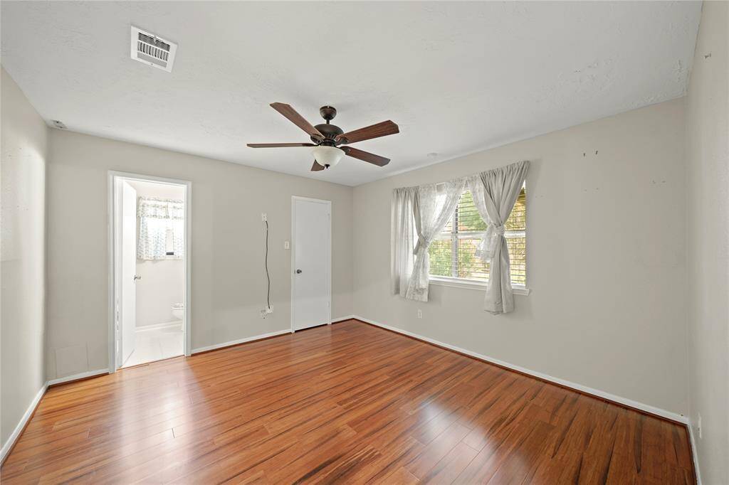 The primary bedroom features wood vinyl floors, a ceiling fan, and a large window  with a view of the backyard. It includes an en-suite bathroom and a walk in  closed.