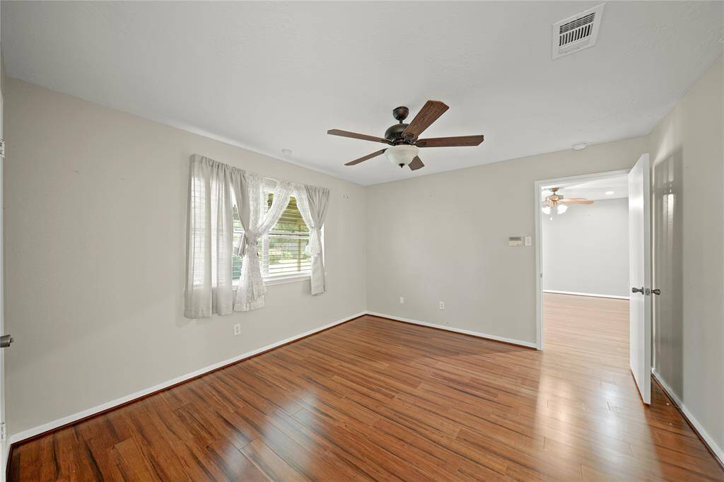 The primary bedroom features wood vinyl floors, a ceiling fan, and a large window  with a view of the backyard. It includes an en-suite bathroom and a walk in  closed.
