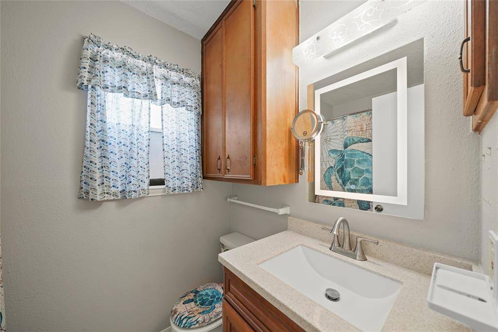 Primary bathroom features a wall-mounted mirror with lighting, and ample wooden cabinetry for storage. The window  provides natural light. There is also a combination shower/tub.