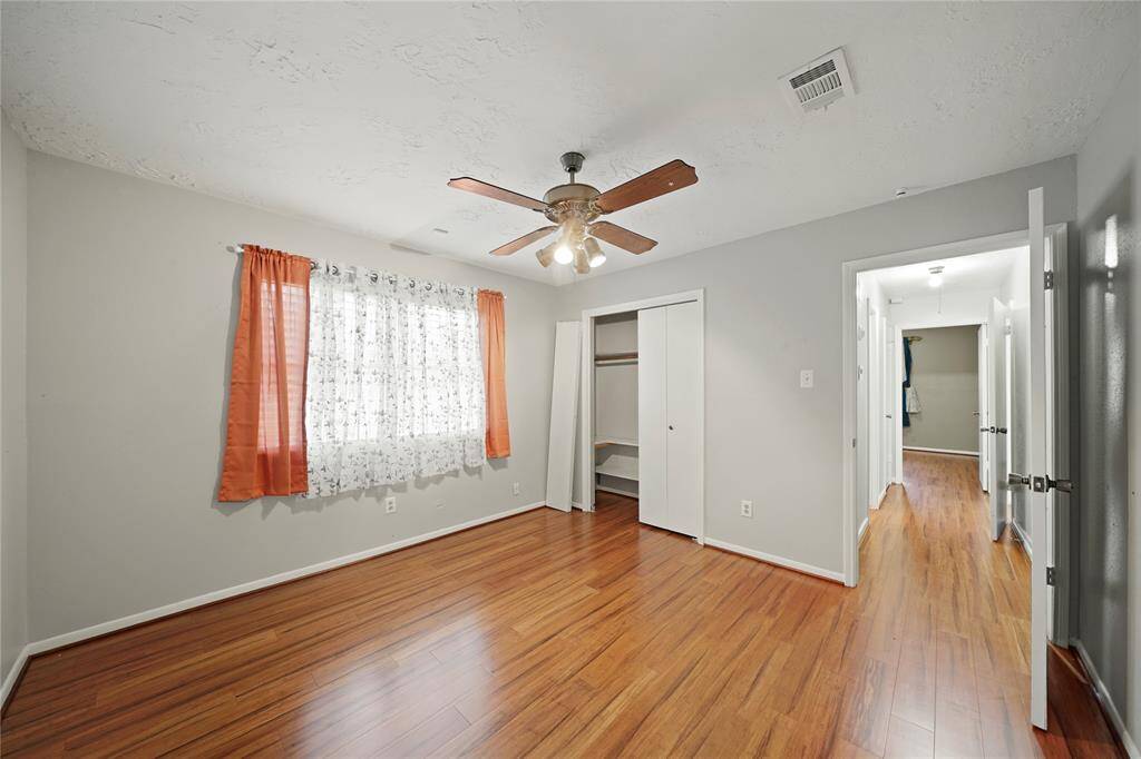 Bedroom located on the opposite side of the house from primary bedroom,  features wood vinyl plank flooring, a ceiling fan and a closet with sliding doors. The space opens to a hallway with another bedroom visible.