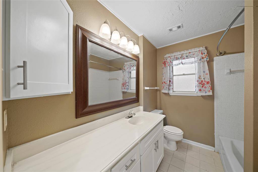 Secondary bathroom located between the two bedroom from the hallway,  features a large mirror above a one sink, white vanity. It has a shower-tub combo and plenty of storage space.
