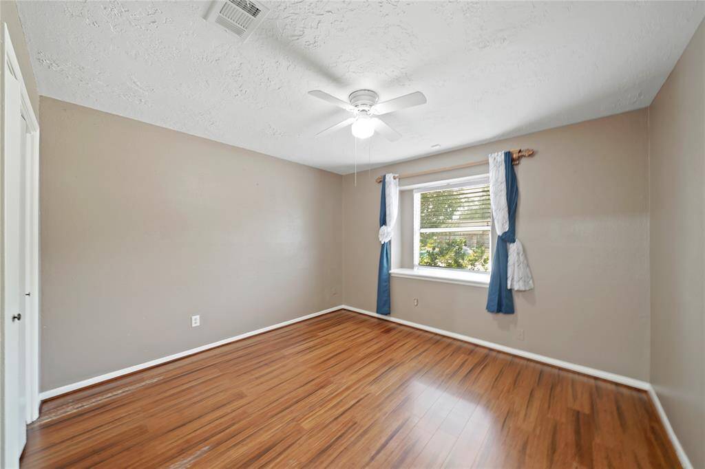 A third bedroom features a ceiling fan, wood like flooring, and a window.