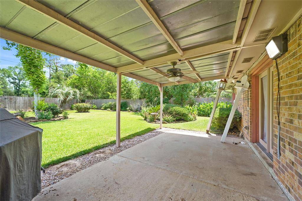 This photo showcases the covered patio with a ceiling fan, providing a shaded outdoor space. It overlooks a well-maintained backyard with lush greenery and a  fence for privacy, perfect for relaxation or entertaining.