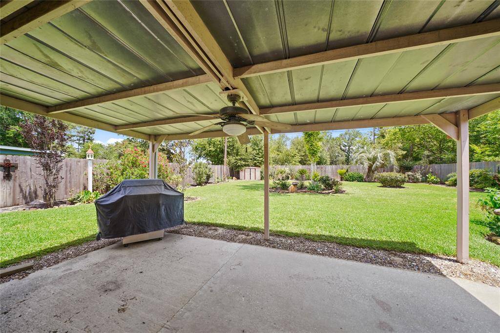 Spacious backyard with a covered patio and ceiling fan overlooking a well-maintained lawn and garden, all enclosed by a wooden fence for privacy.