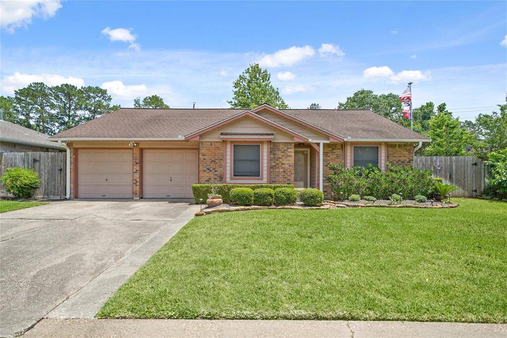 This charming brick home features a well-maintained front yard with lush greenery, a two-car garage, and a welcoming entrance. The property is framed by a wooden fence, offering privacy.