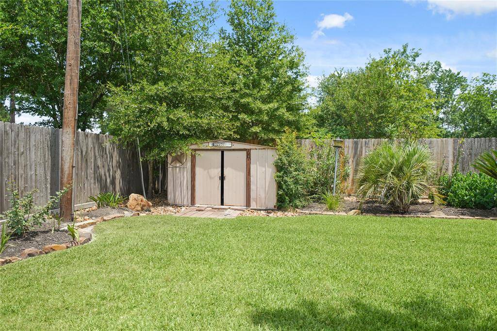 Spacious backyard with well-maintained lawn, lush greenery, and a wooden storage shed, perfect for outdoor activities and storage needs.