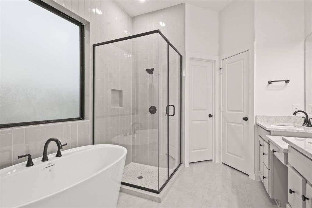 Spa bathroom with a grand freestanding bathtub lined in the utmost stylish manner with tile to the ceiling. Paired perfectly with quartz countertops and modern black hardware.