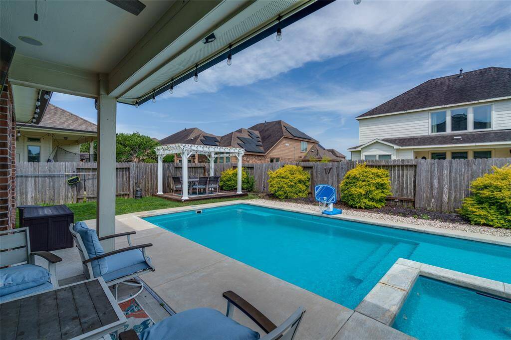 Step into your private backyard oasis featuring a spacious covered patio, sparkling pool, relaxing hot tub, and an additional patio area shaded by a charming pergola—perfect for entertaining and unwinding in style.