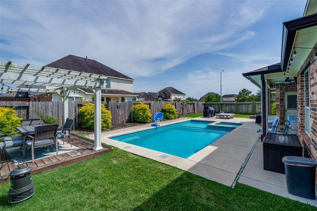 Step into your private backyard oasis featuring a spacious covered patio, sparkling pool, relaxing hot tub, and an additional patio area shaded by a charming pergola—perfect for entertaining and unwinding in style.