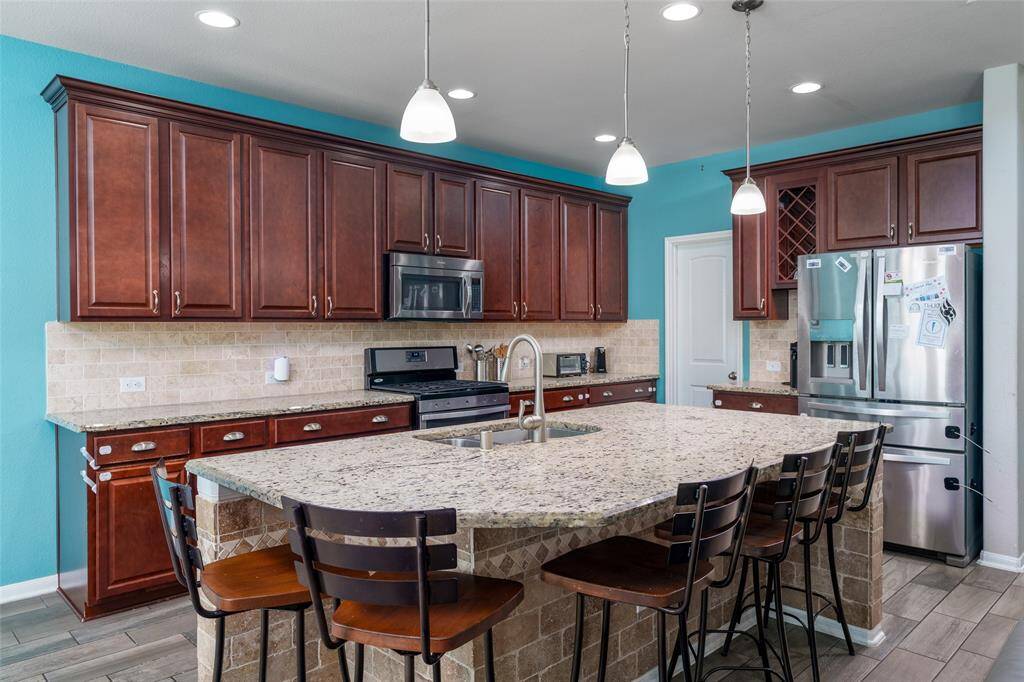 The kitchen impresses with rich brown stained cabinets, sleek granite countertops, a spacious island perfect for meal prep or gatherings, and a stylish backsplash that ties the whole space together with elegance.