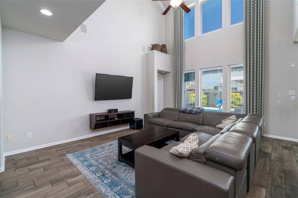 The stunning living room boasts ultra high ceilings, a sleek ceiling fan, and a dramatic wall of windows with privacy blinds that flood the space with natural light while maintaining comfort and elegance.