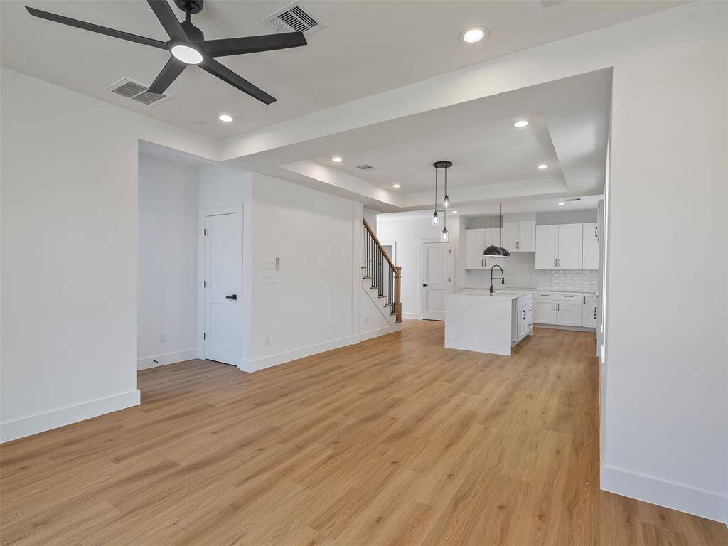Modern, open-concept living area with light wood flooring, a sleek ceiling fan, and recessed lighting. The kitchen features a central island with a marble countertop, white cabinetry, and stylish pendant lights, creating a bright and inviting atmosphere.