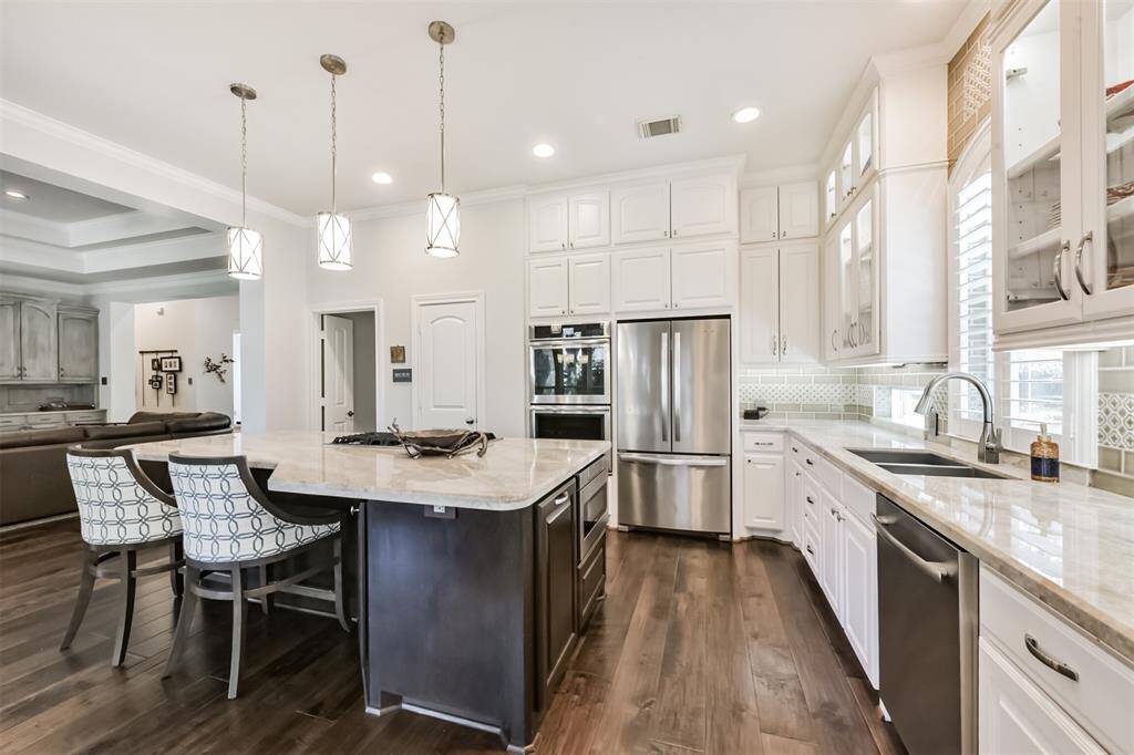 This kitchen features sleek stainless steel appliances, ample white cabinetry, and a large central island with stylish pendant lighting. The open layout flows into the living area, creating a spacious and inviting atmosphere.