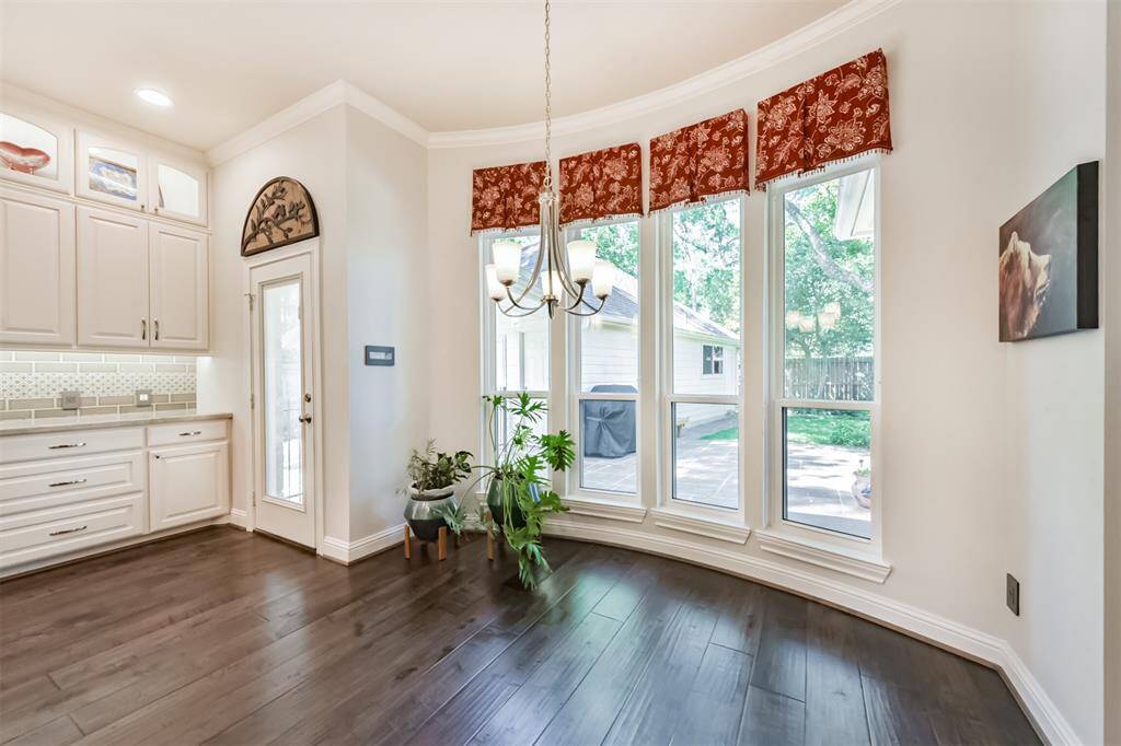 Bright dining area with large windows offering a view of the backyard. Features hardwood floors, elegant cabinetry, and a modern light fixture. Includes a door leading to an outdoor patio.