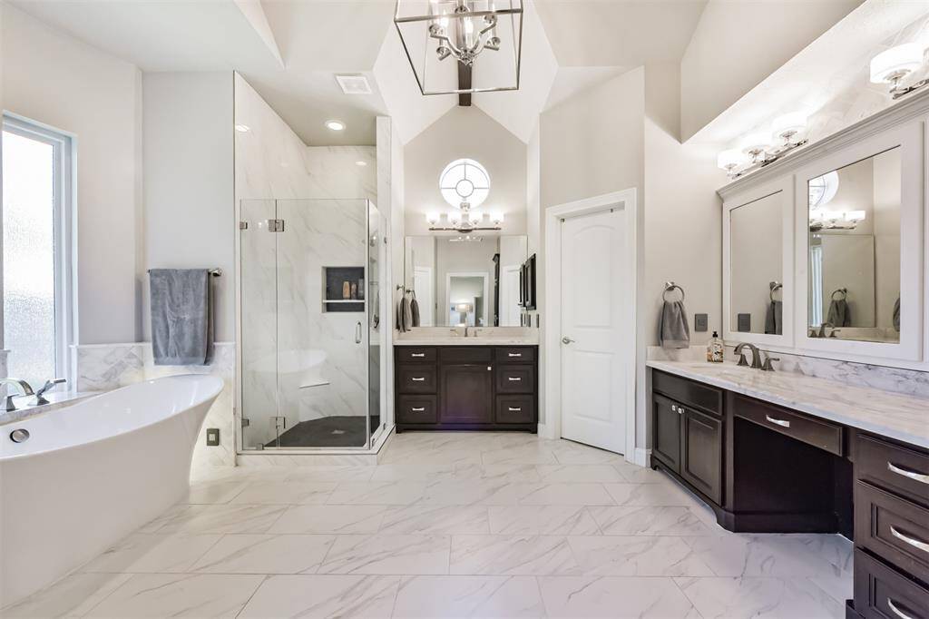This spacious bathroom features a modern design with a freestanding bathtub, a glass-enclosed shower, and dual vanities with elegant marble countertops. High ceilings and ample natural light enhance its luxurious feel.