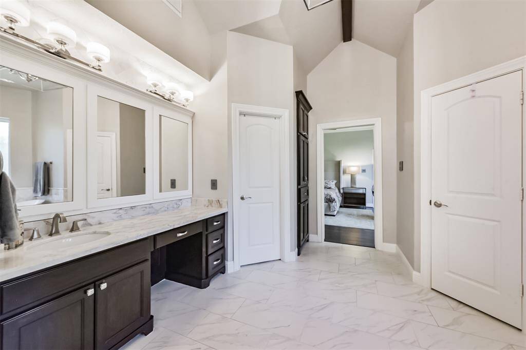 This spacious bathroom features a double vanity with elegant marble countertops, ample storage, and modern light fixtures. The room has high ceilings and opens into a bedroom, offering a seamless flow and a luxurious feel.