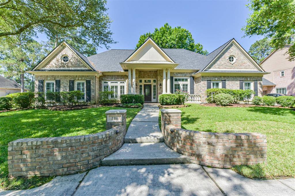 This photo shows a charming, single-story brick home with a symmetrical facade, large windows, and neatly manicured landscaping. It features a welcoming front porch supported by columns and a curved brick pathway leading to the entrance. The property is surrounded by mature trees, offering a serene and inviting atmosphere.