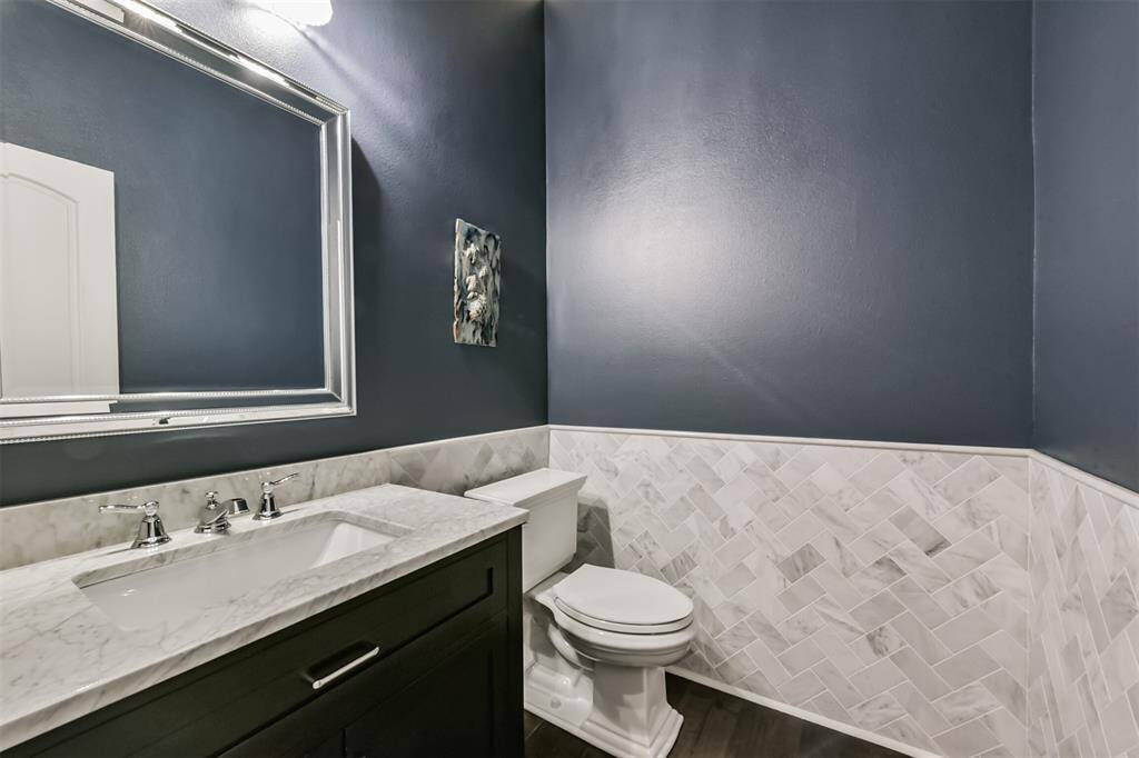 This is a stylish bathroom featuring dark blue walls with elegant white wainscoting in a herringbone pattern. It includes a modern vanity with a marble countertop and a sleek framed mirror, creating a sophisticated and clean look.