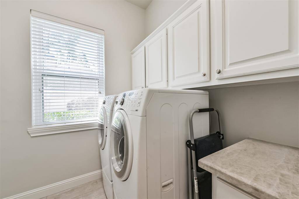 This laundry room features a modern washer and dryer set beneath a window that provides natural light. It includes white cabinetry for storage and a folding counter for convenience.