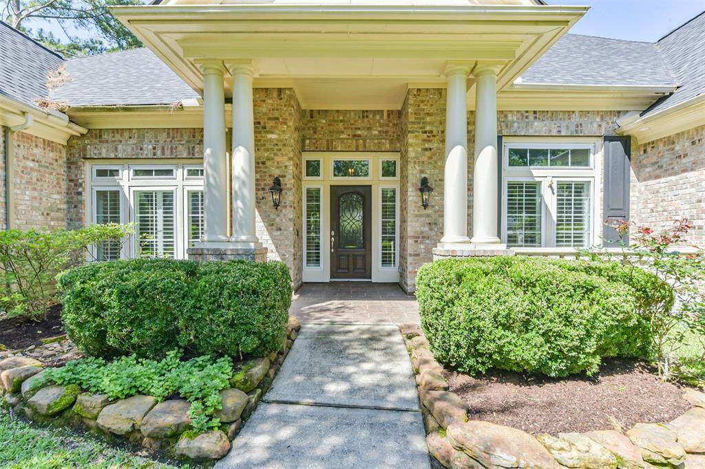 inviting front entrance with elegant columns and a brick facade. The pathway is lined with well-maintained shrubs and landscaping, leading to a classic door with decorative glass. Abundant windows with shutters add charm and natural light.