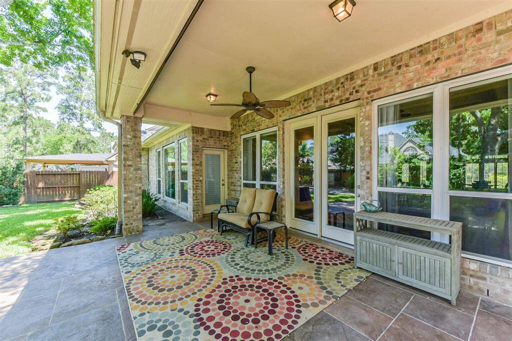 This inviting patio features a spacious, covered area with ceiling fans, comfortable seating, and large windows overlooking a lush backyard. Perfect for relaxing or entertaining.