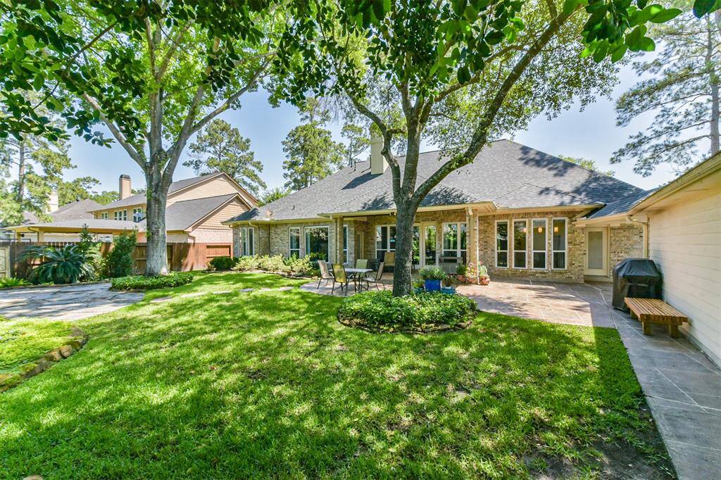 Charming backyard with lush greenery and mature trees, offering a spacious patio area perfect for outdoor entertaining. The house features large windows and a classic brick exterior, creating a welcoming and serene atmosphere.